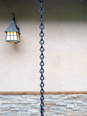Long section of black droplet rain chain connected to installation kit