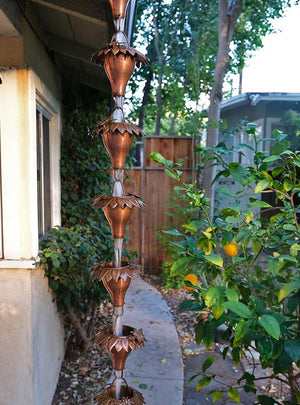 Sunflower Copper Rain Chain hanging from a gutter in a garden