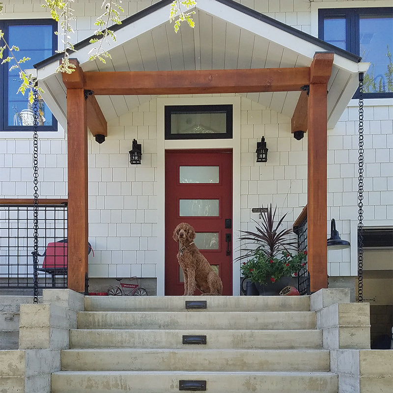 Two Double Loops Rain Chains hanging from an entry way on a white house with a dog in front of the front door. 