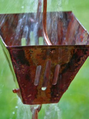 close up of Aged copper Slotted Square Cups Rain Chain with water flowing through a cup