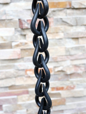 Section of black droplet rain chain against stone wall