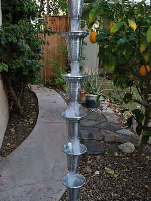 Flared Cups Rain Chain in Aluminum with water flowing through multiple cups during rainstorm