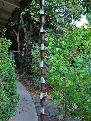 Bronze Honeysuckle Rain Chain hanging from a gutter in a garden