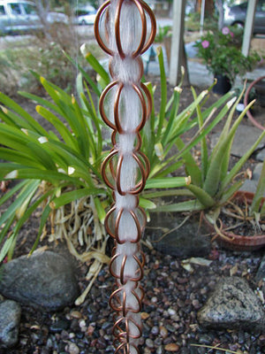 Full length image of Triple Loops 2.5-inch Copper Link Rain Chain with water running through it